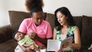 A mother holds her baby as another woman goes over safe sleep materials.